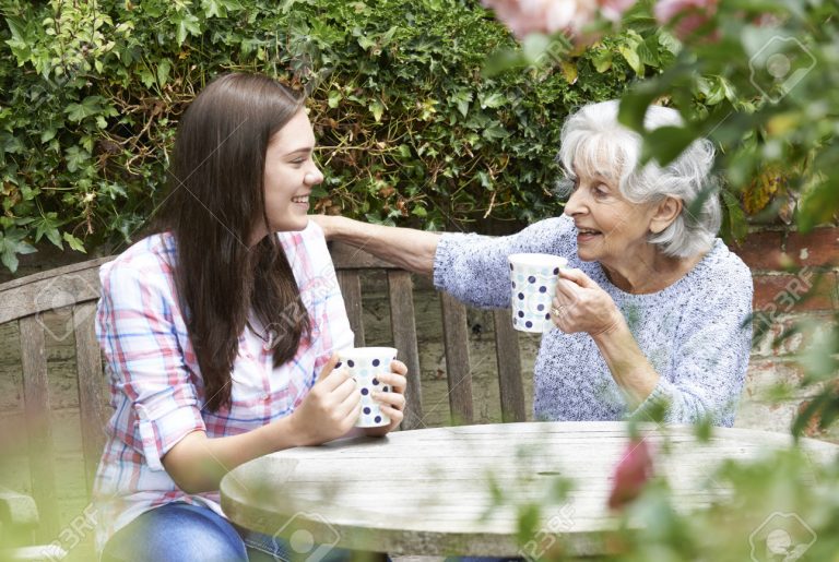 Teenage Granddaughter Relaxing With Grandmother In Garden